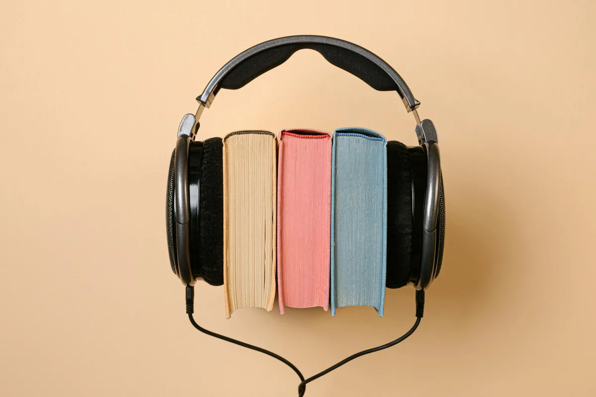 Headphones with colorful books arranged in the center, representing audiobooks or literary content on a beige background.