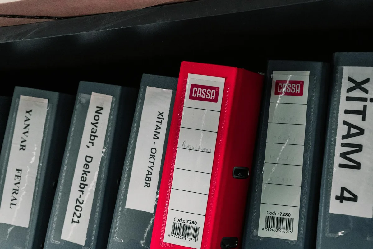 Row of cash register books with gray and red covers, labeled with dates and product codes on white labels.