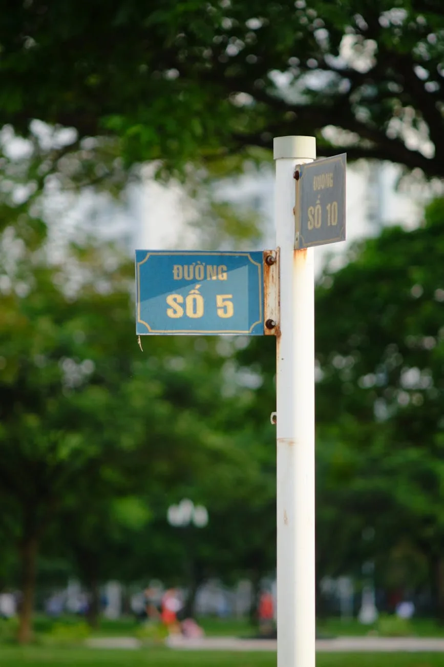 Vietnamese street sign showing "Đường số 5" and "Số 10" on white pole with blooming trees in background