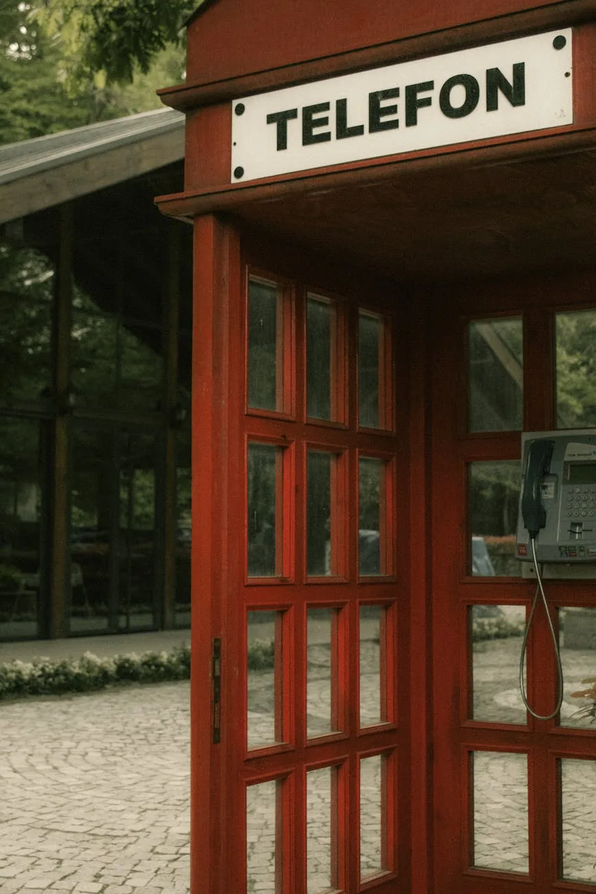 Red telephone booth with "TELEFON" sign in a wooded area next to a brick building.
