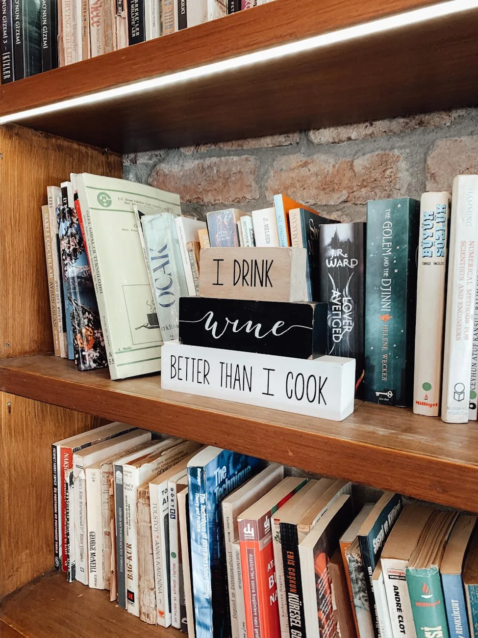 Wooden bookshelf with books and decorative signs reading "I drink wine better than I cook"