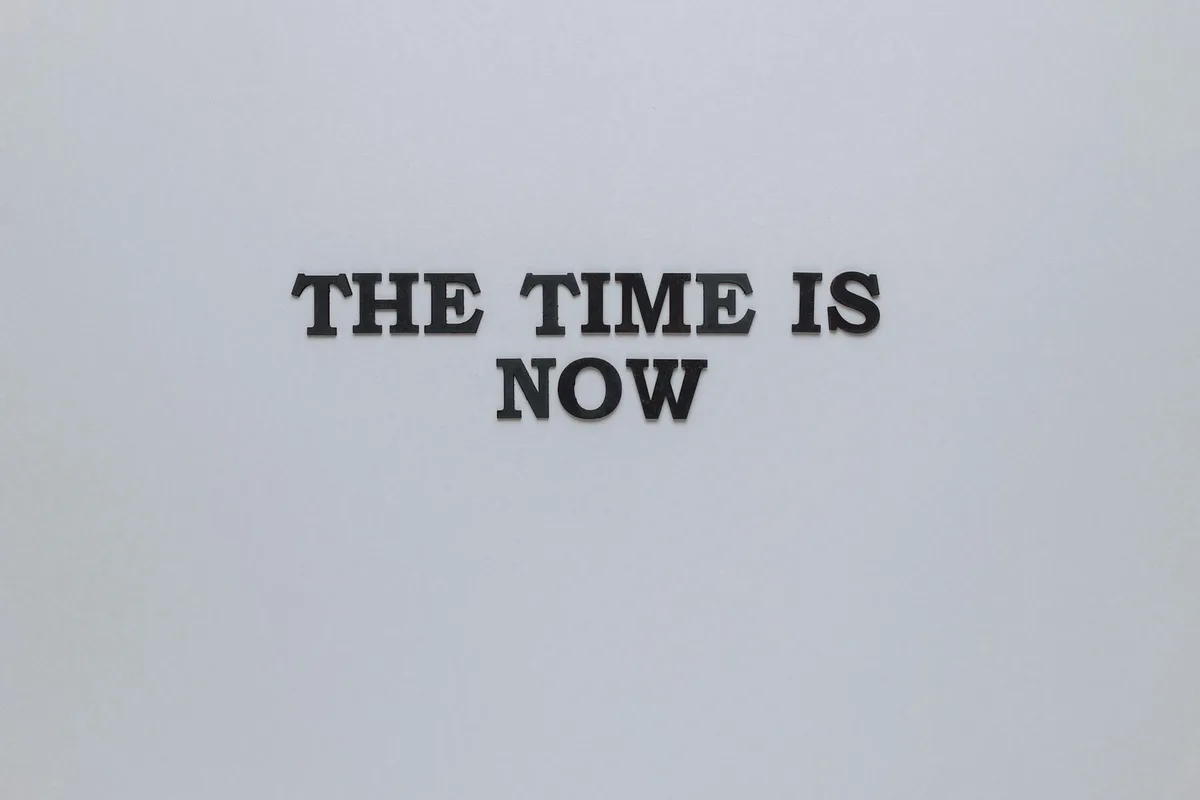 Black text reading "THE TIME IS NOW" on a light gray background