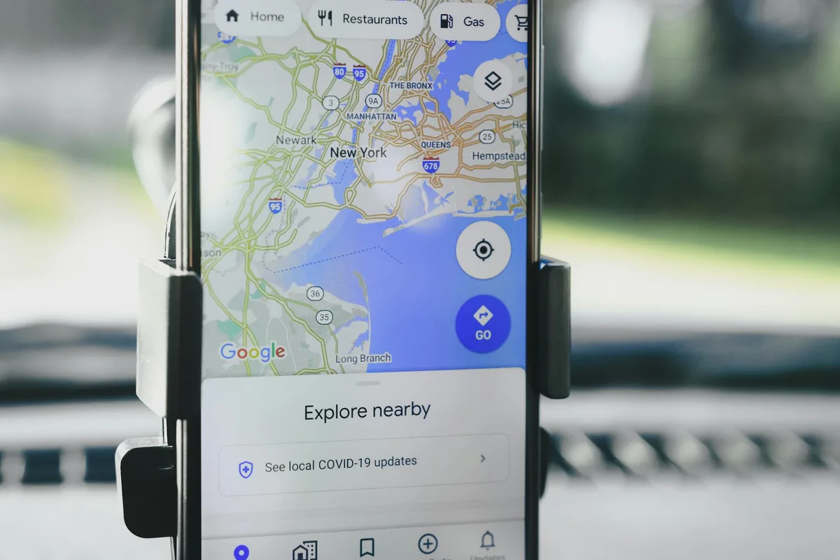 Google Maps app showing New York City area with navigation options, restaurants, and gas stations visible on smartphone in car mount.