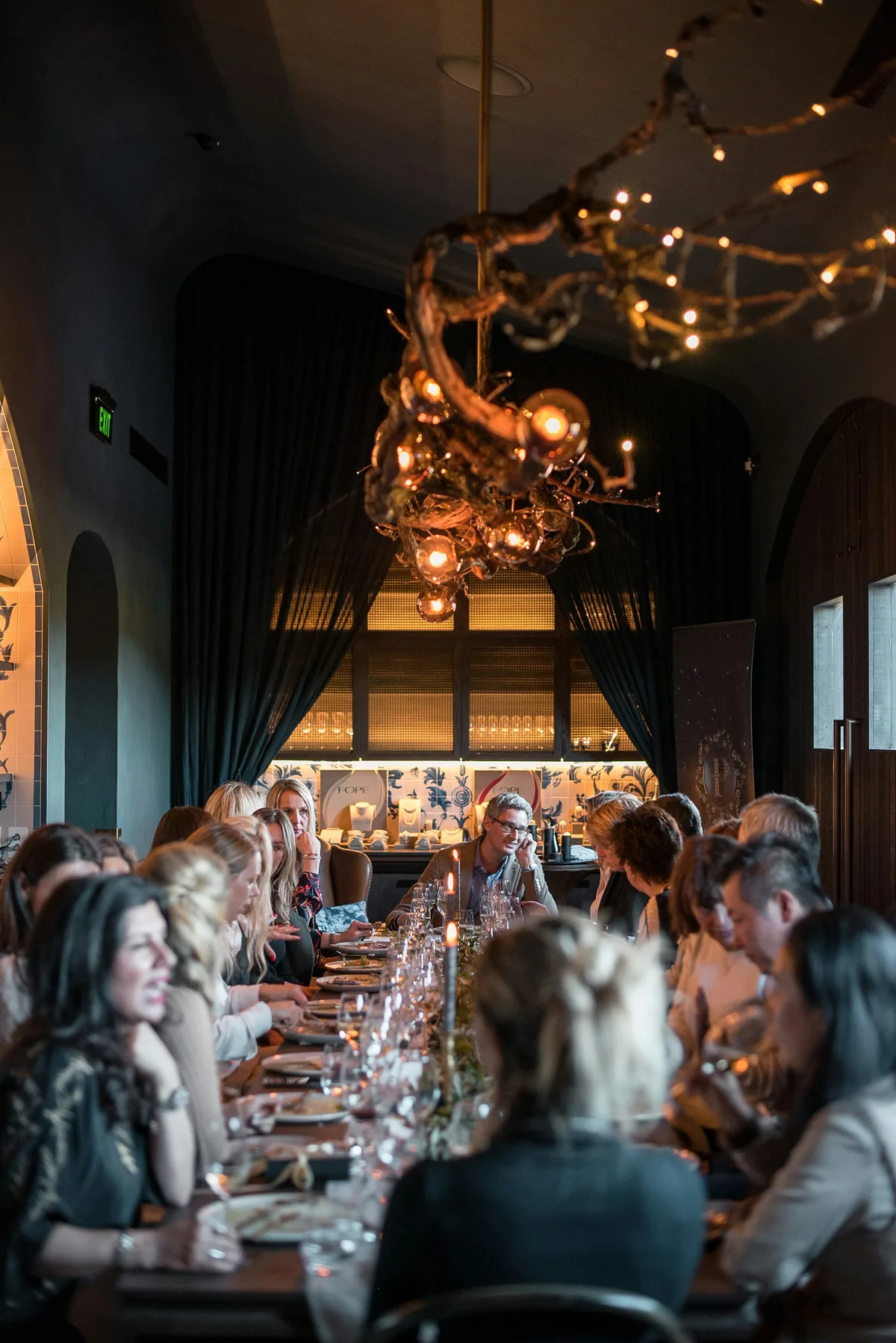 A group of people gathered around a long dinner table lit by warm candlelight