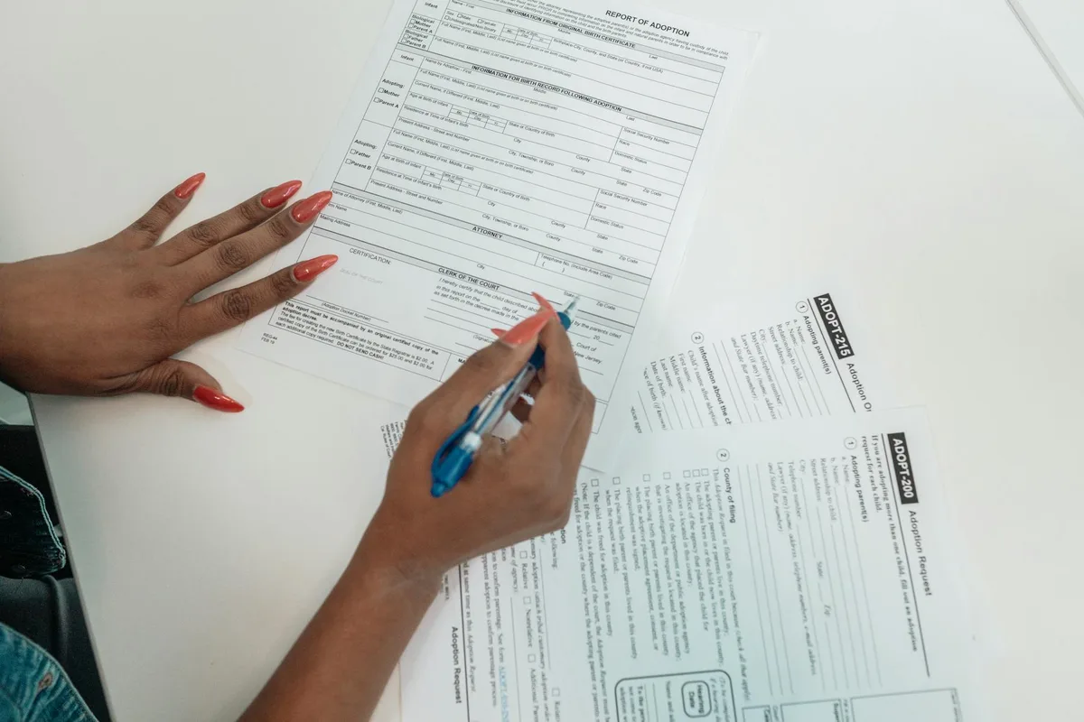 Person filling out a Report of Adoption legal document with a blue pen
