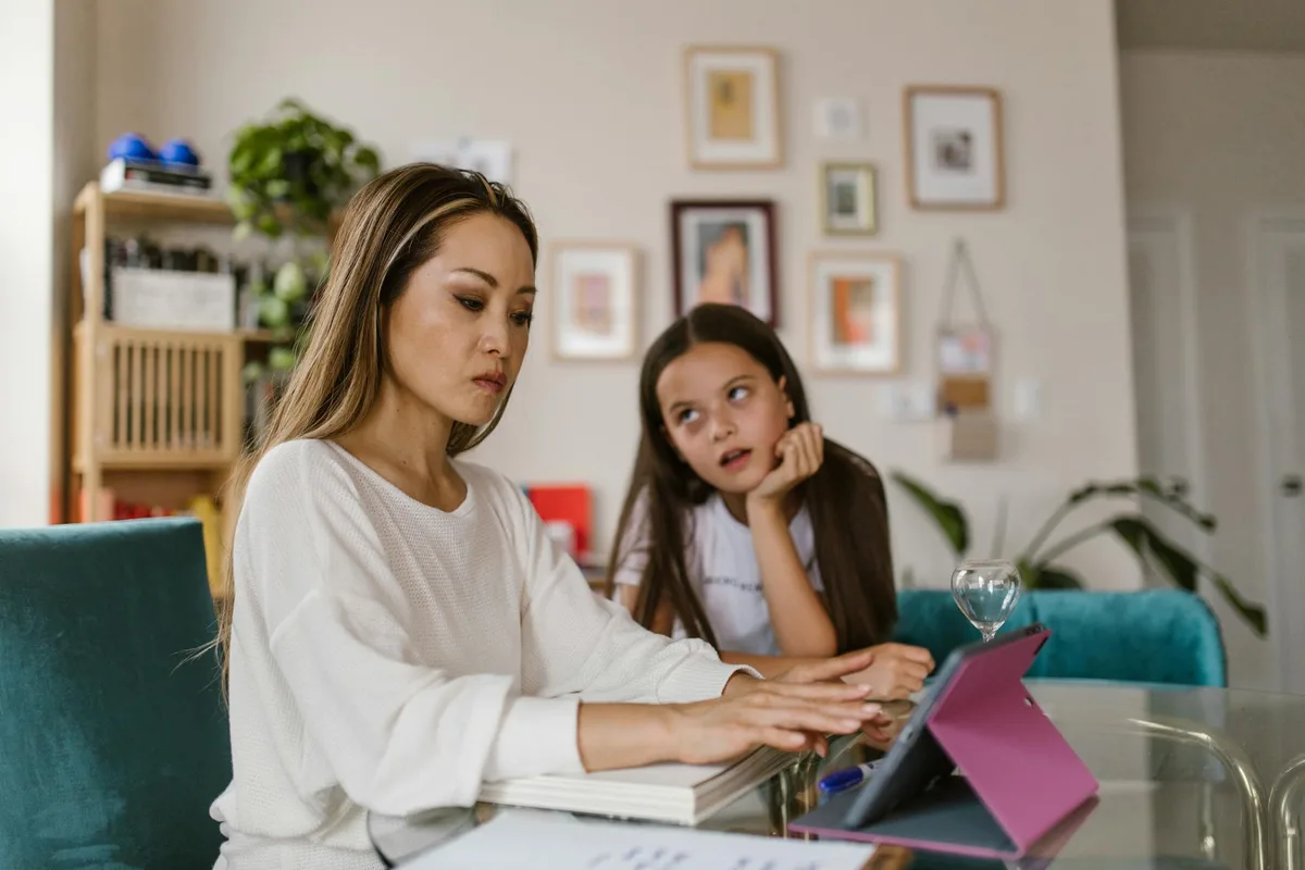 Mother and daughter sitting at table working on laptop together in home office setting